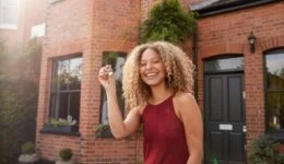 Portrait Of Excited Young Woman Standing Outside New Home Holding Keys