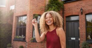 Portrait Of Excited Young Woman Standing Outside New Home Holding Keys