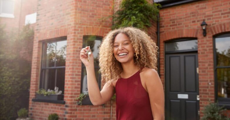 Portrait Of Excited Young Woman Standing Outside New Home Holding Keys