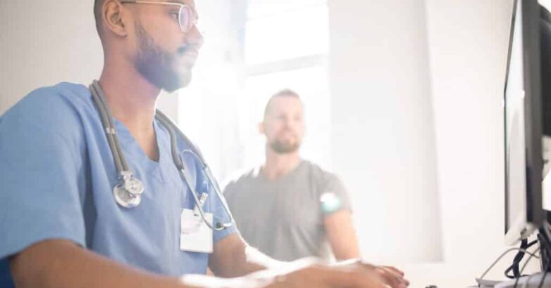 Serious doctor filling in electronic document with data of patient by computer