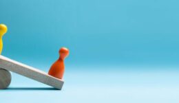 Red And Yellow Pawns Figures Balancing On Wooden Seesaw